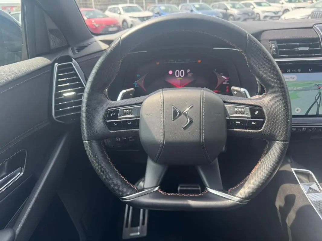 Vue intérieure centrée sur le volant noir perforé du DS7 E-Tense 2024 avec tableau de bord numérique et écran tactile.