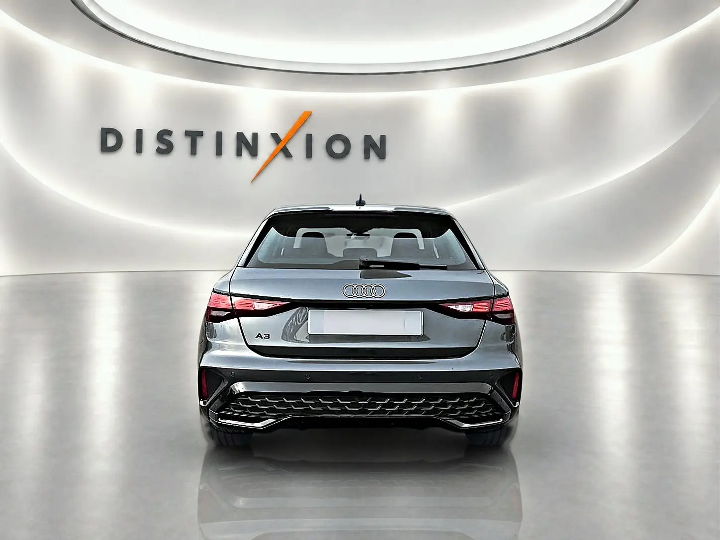 Vue arrière d'une Audi A3 Sportback gris Daytona avec feux LED et becquet arrière dans un showroom lumineux.