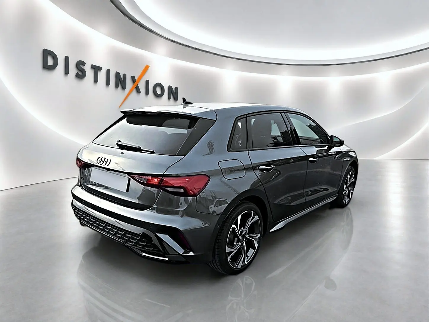 Audi A3 Sportback gris Daytona vue 3/4 arrière droit dans un showroom lumineux avec jantes alu graphiques.