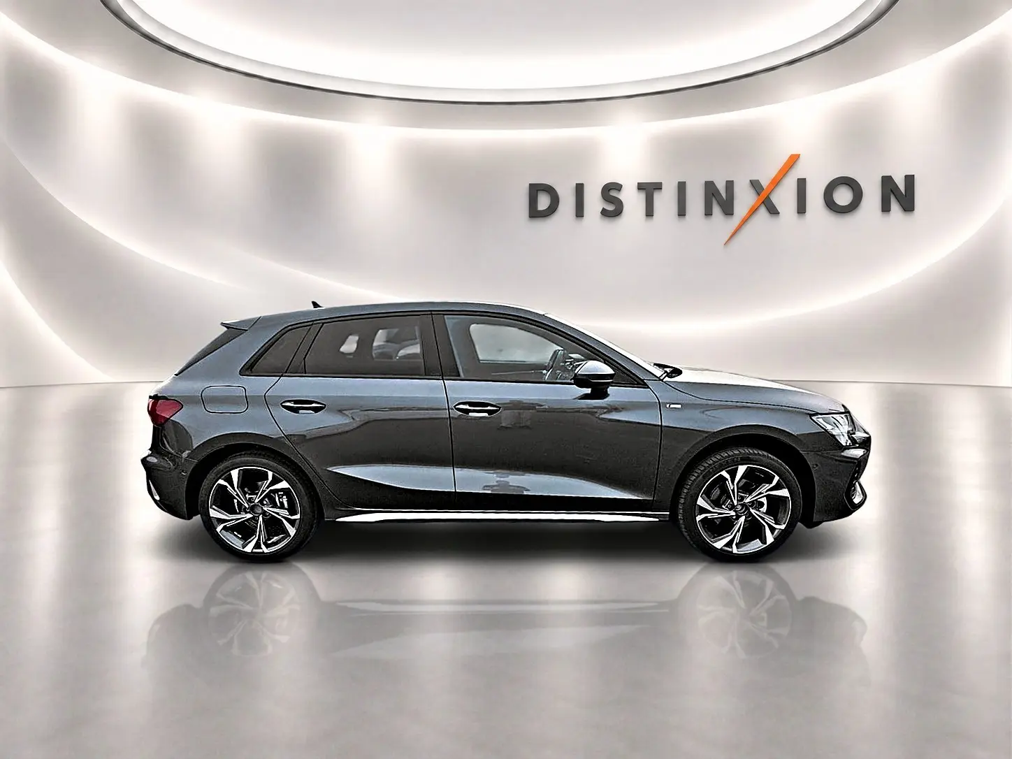 Profil droit d'une Audi A3 Sportback gris Daytona 2026 avec jantes alu et finition S line dans un showroom lumineux.
