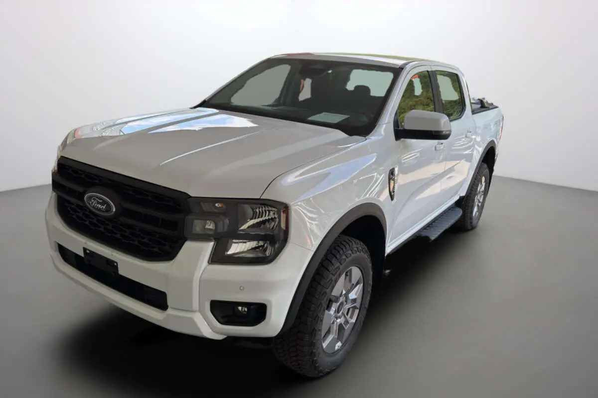Ford Ranger blanc glacier en 3/4 avant droit, avec calandre noire et jantes alu 18 pouces tout terrain.