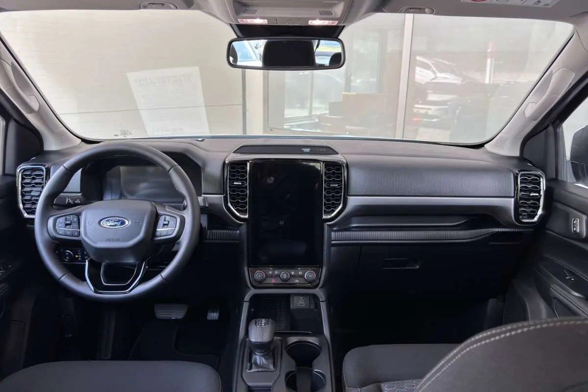 Vue intérieure avant du Ford Ranger 2.3 PHEV, tableau de bord noir avec écran tactile vertical et volant multifonctions.