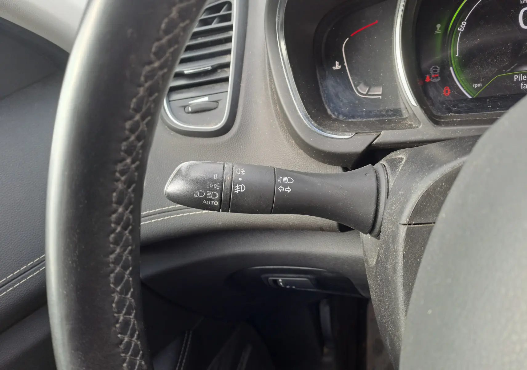Gros plan sur la commande des feux et clignotants à gauche du volant noir dans l'habitacle gris du Renault Scenic IV.