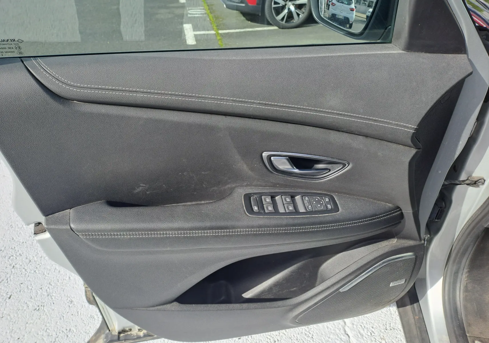 Porte avant gauche ouverte d'un Renault Scenic IV gris platine, montrant la garniture intérieure noire avec commandes électriques.