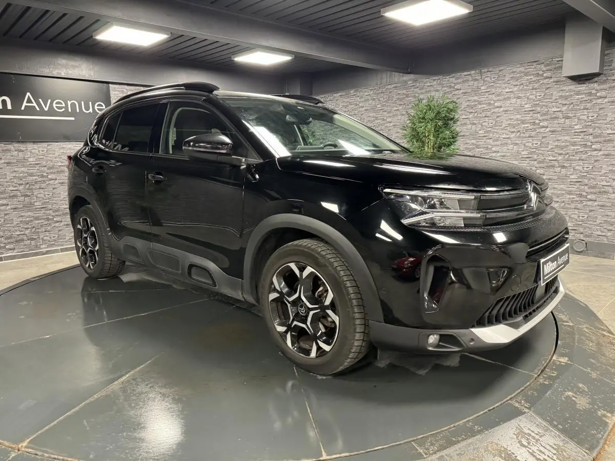 Vue 3/4 avant d'un Citroën C5 Aircross noir nacré avec jantes bi-ton et barres de toit noir brillant.