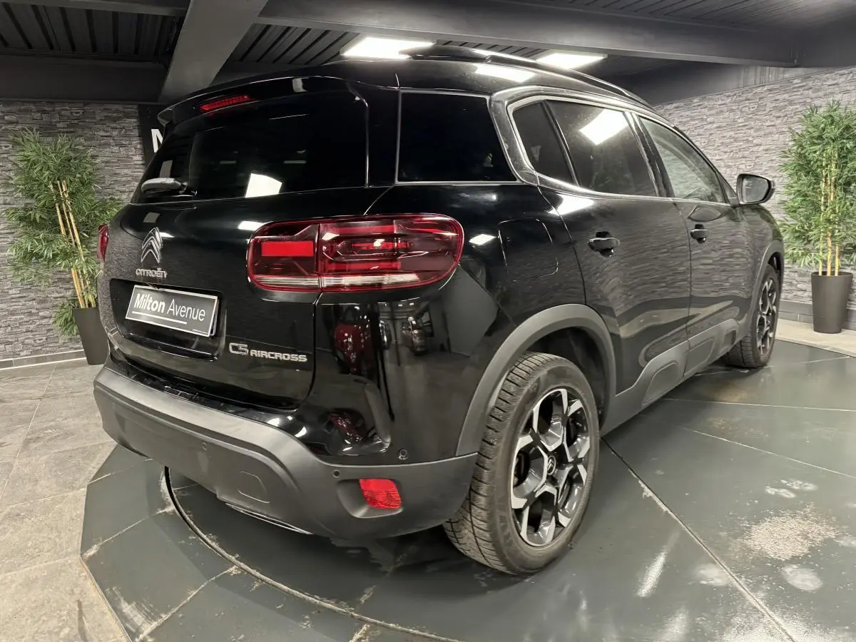 Vue 3/4 arrière droite du Citroën C5 Aircross noir nacré avec jantes bi-ton et barres de toit noires.