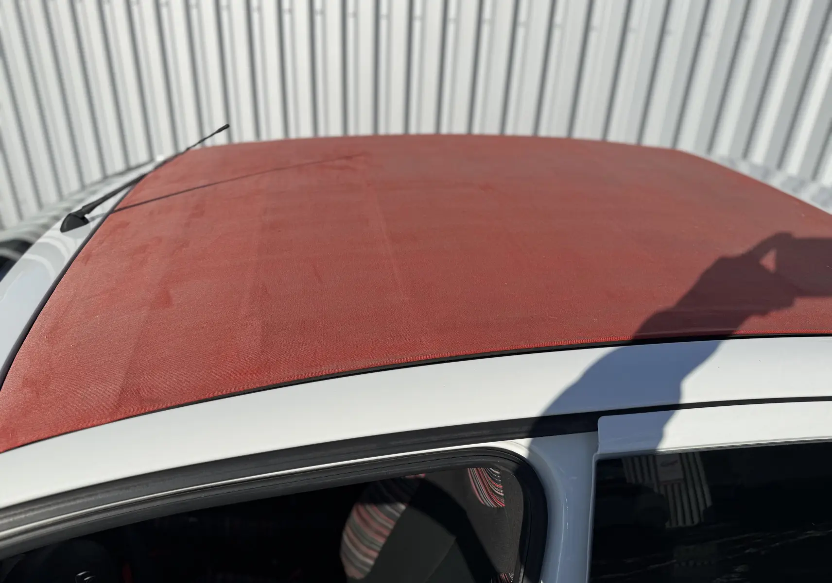 Toit ouvrant rouge en toile sur une Citroën C1 blanche vue de dessus côté gauche, avec antenne arrière visible.