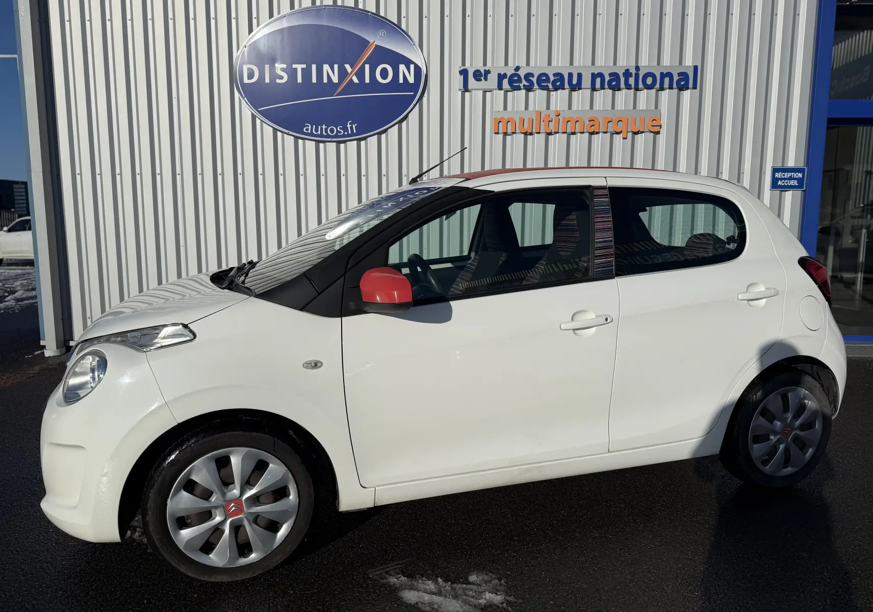 Vue latérale gauche d'une Citroën C1 blanche 2014 avec rétroviseurs rouges et jantes argentées en extérieur.