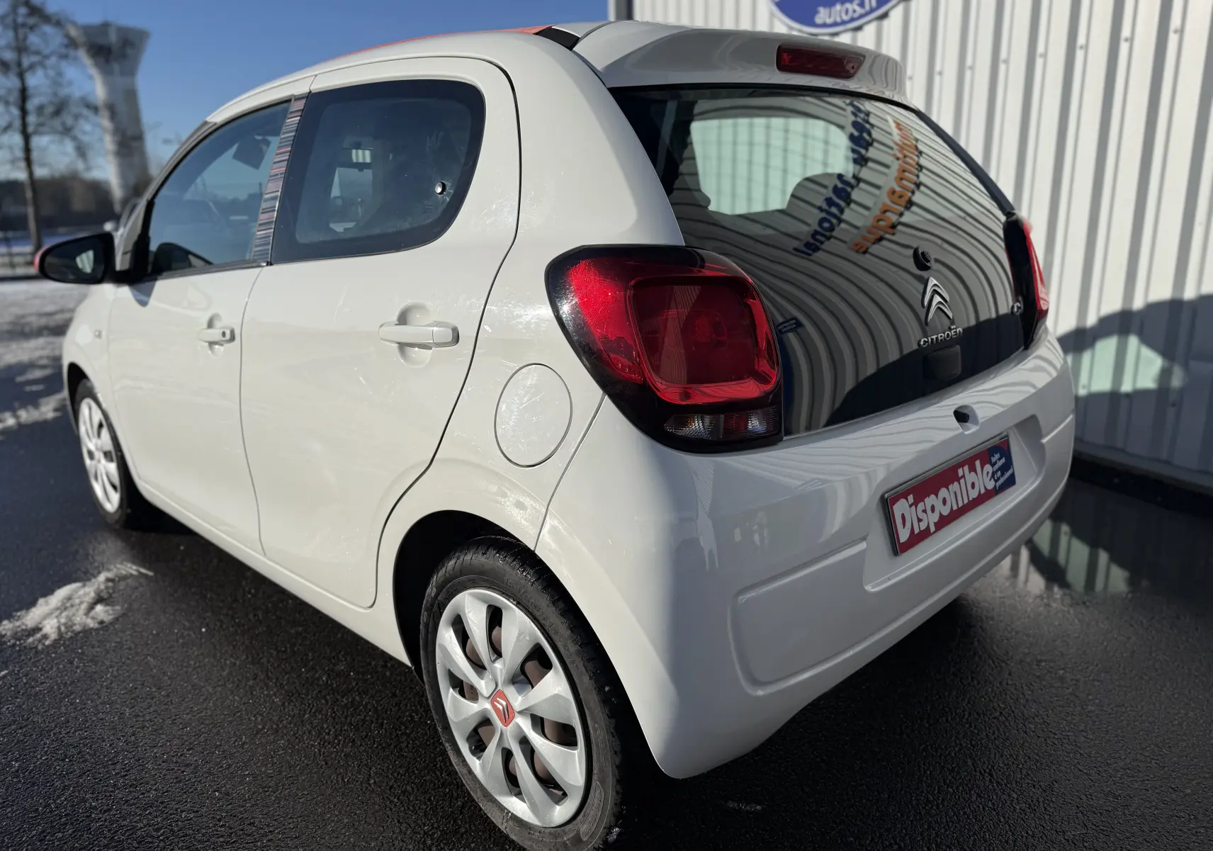 Vue 3/4 arrière droite d'une Citroën C1 blanche 2014 avec feux arrière rouges et jantes alliage.