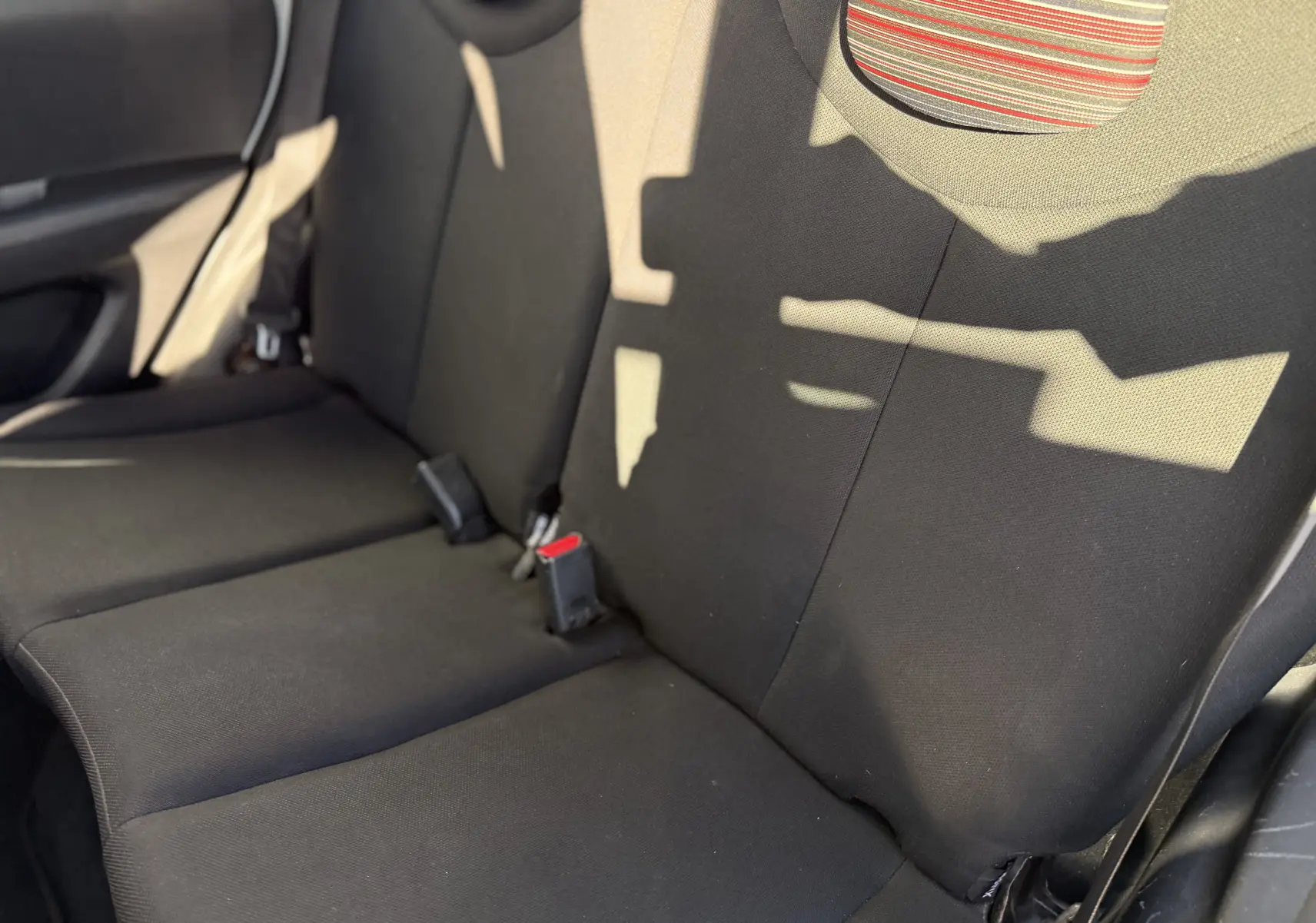 Vue rapprochée des sièges arrière en tissu noir de la Citroën C1 2014, avec appuie-tête à rayures colorées.