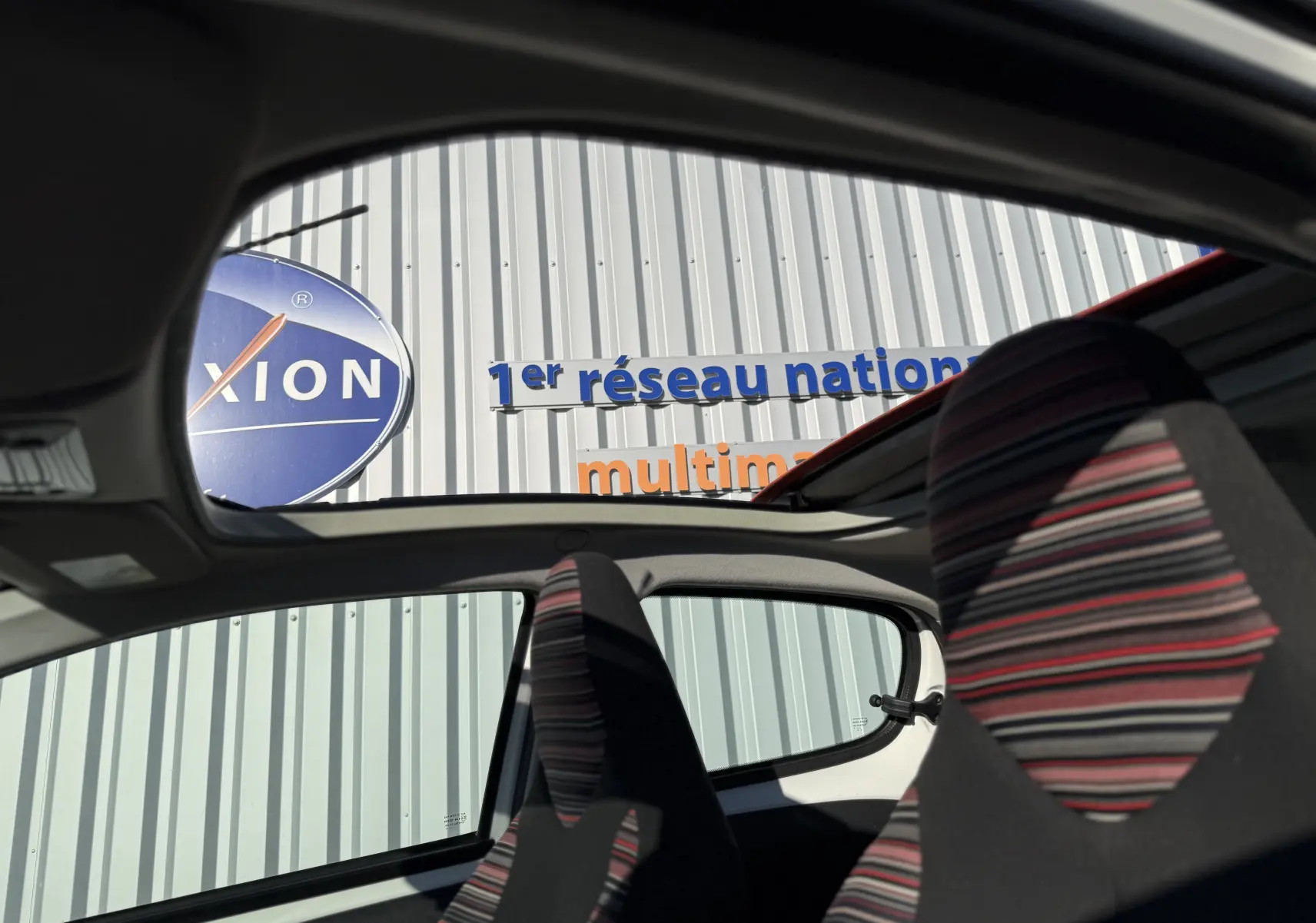 Vue intérieure de la Citroën C1 blanche 2014, montrant les sièges avant à motifs rayés et le toit ouvrant panoramique.