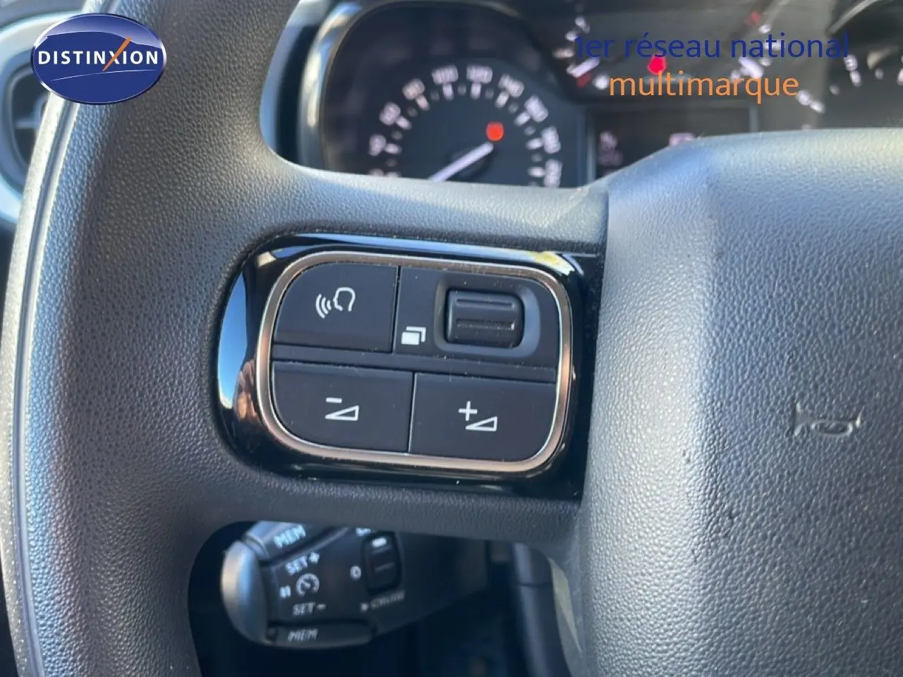 Gros plan sur les commandes au volant à gauche du Citroën C3 2020, intérieur noir avec tableau de bord flou en arrière-plan.