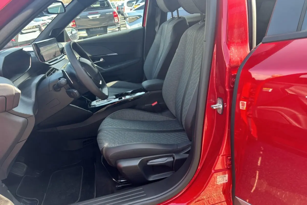Vue intérieure côté conducteur d'un Peugeot 2008 rouge elixir 2025, avec sièges tissu et tableau de bord moderne.