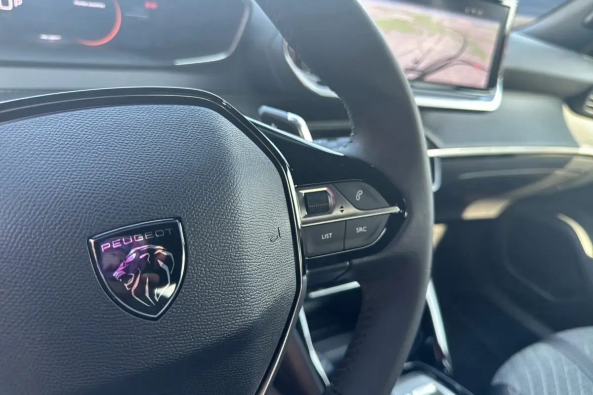 Gros plan sur le volant cuir multifonctions Peugeot 2008 Hybrid 145, avec tableau de bord et écran tactile en arrière-plan.