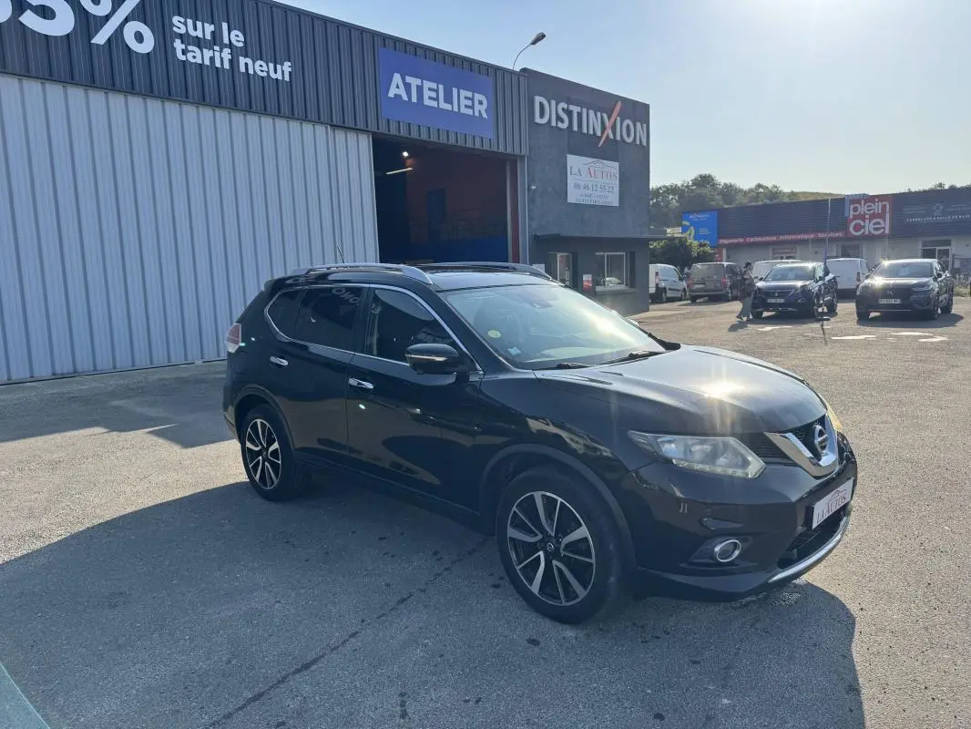 Nissan X-TRAIL III noir vu en 3/4 avant droit, avec jantes alliage et toit ouvrant, stationné devant un atelier.