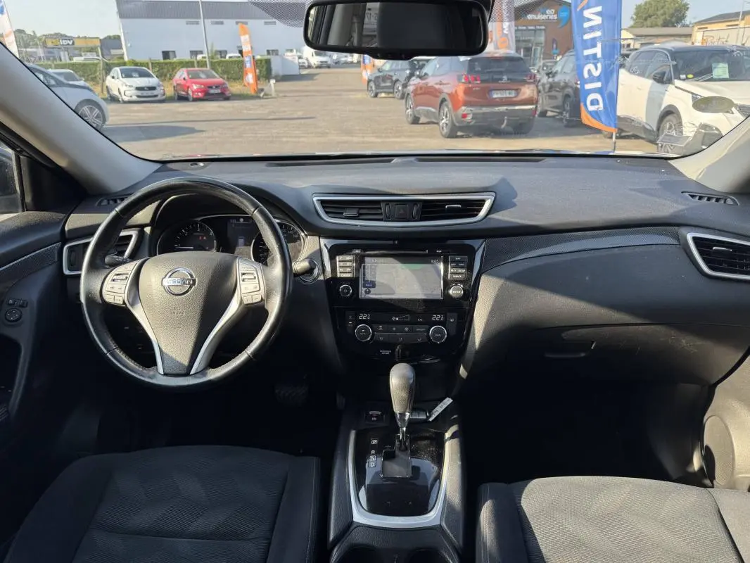 Vue intérieure avant du Nissan X-TRAIL noir 2017, montrant le volant, la console centrale avec écran tactile et levier de boîte automatique.