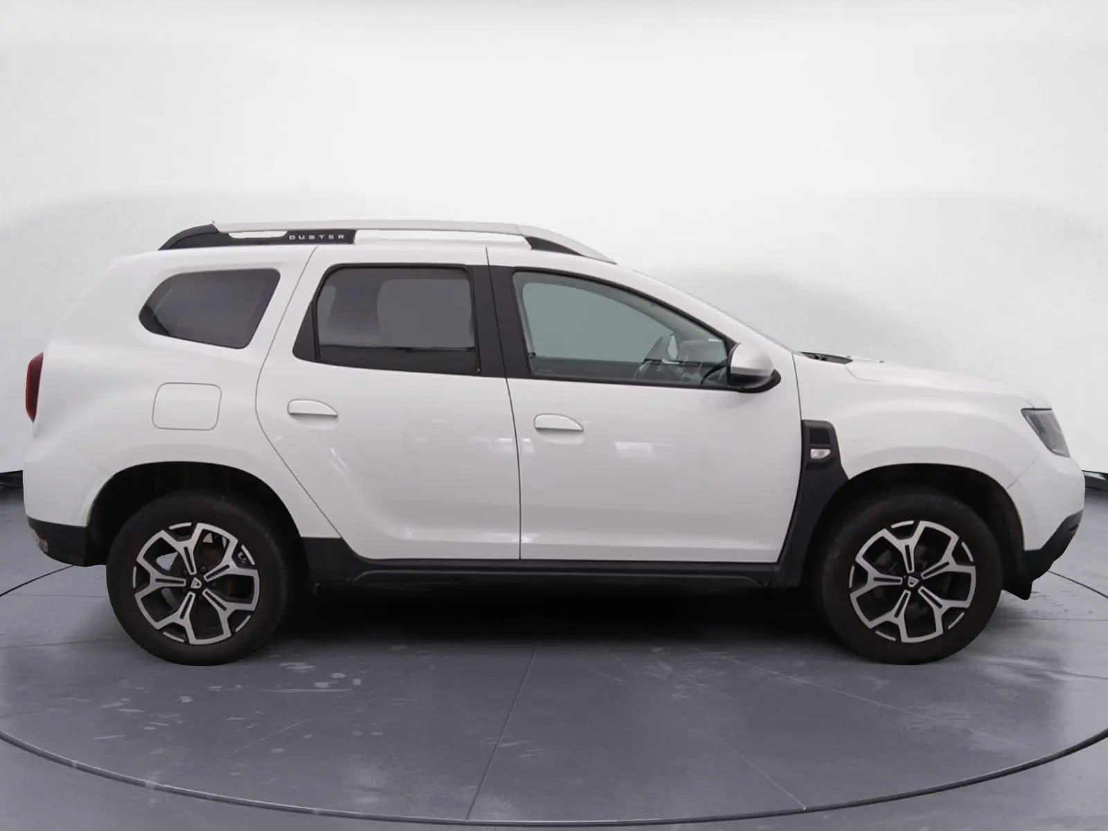 Profil droit d'un Dacia Duster blanc 2021 avec jantes alliage noires et toit noir, stationné sur un sol gravillonné.