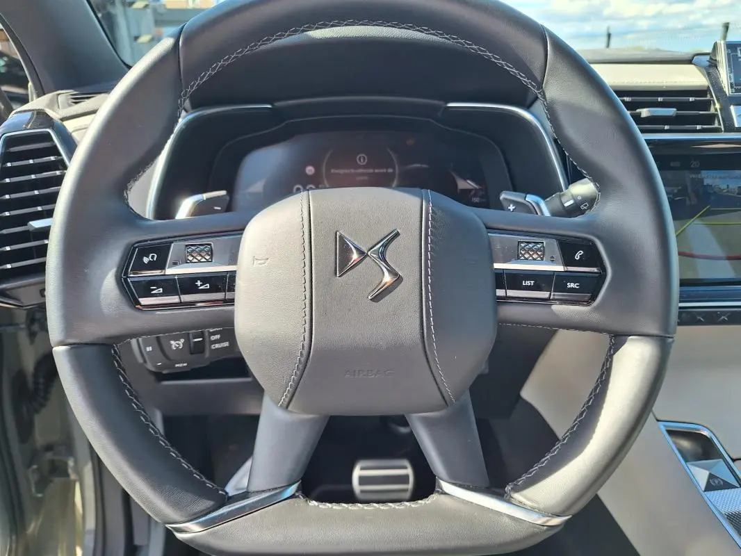 Vue rapprochée du volant en cuir noir du DS7 2024, avec commandes intégrées et tableau de bord numérique en arrière-plan.
