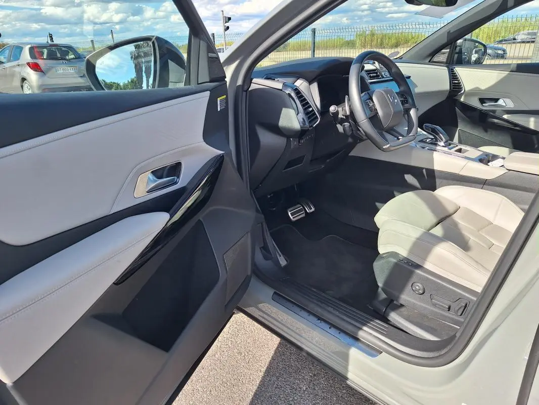 Intérieur clair vu côté conducteur d’un DS7 gris 2024, avec volant multifonction et sièges cuir beige.