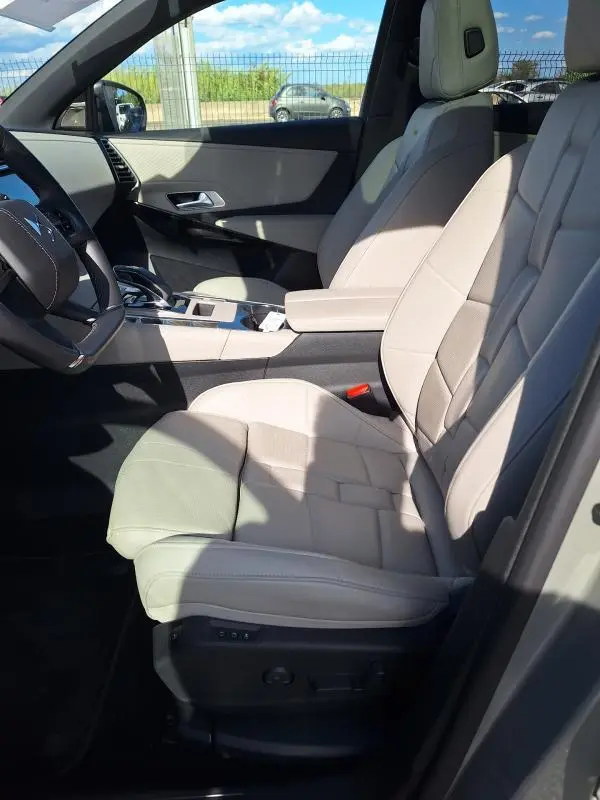 Vue intérieure côté conducteur du DS7 2024, sièges cuir beige, accoudoir central et volant multifonction.
