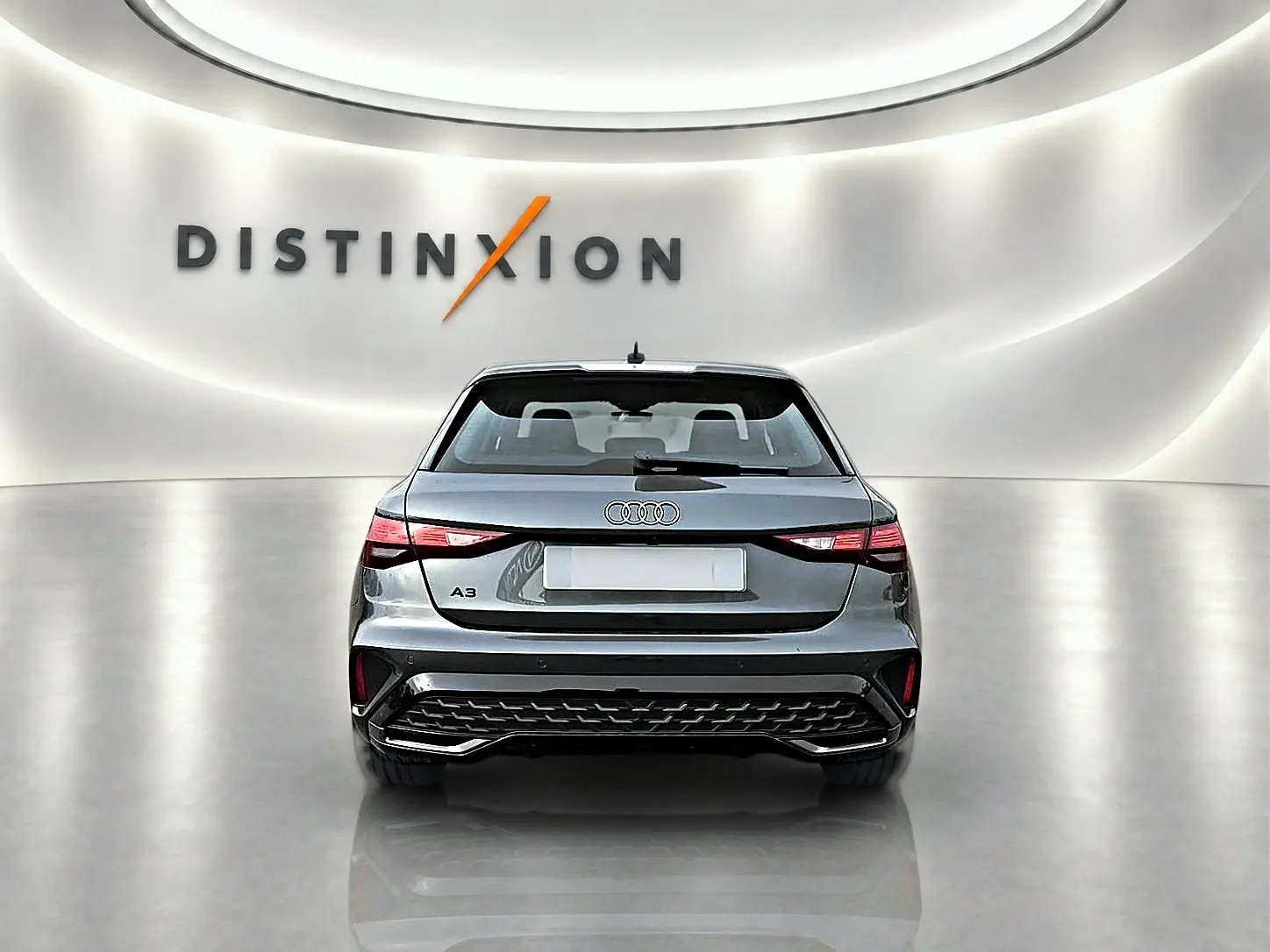 Vue arrière d'une Audi A3 Sportback gris Daytona 2026 avec feux LED et diffuseur noir dans un showroom lumineux.