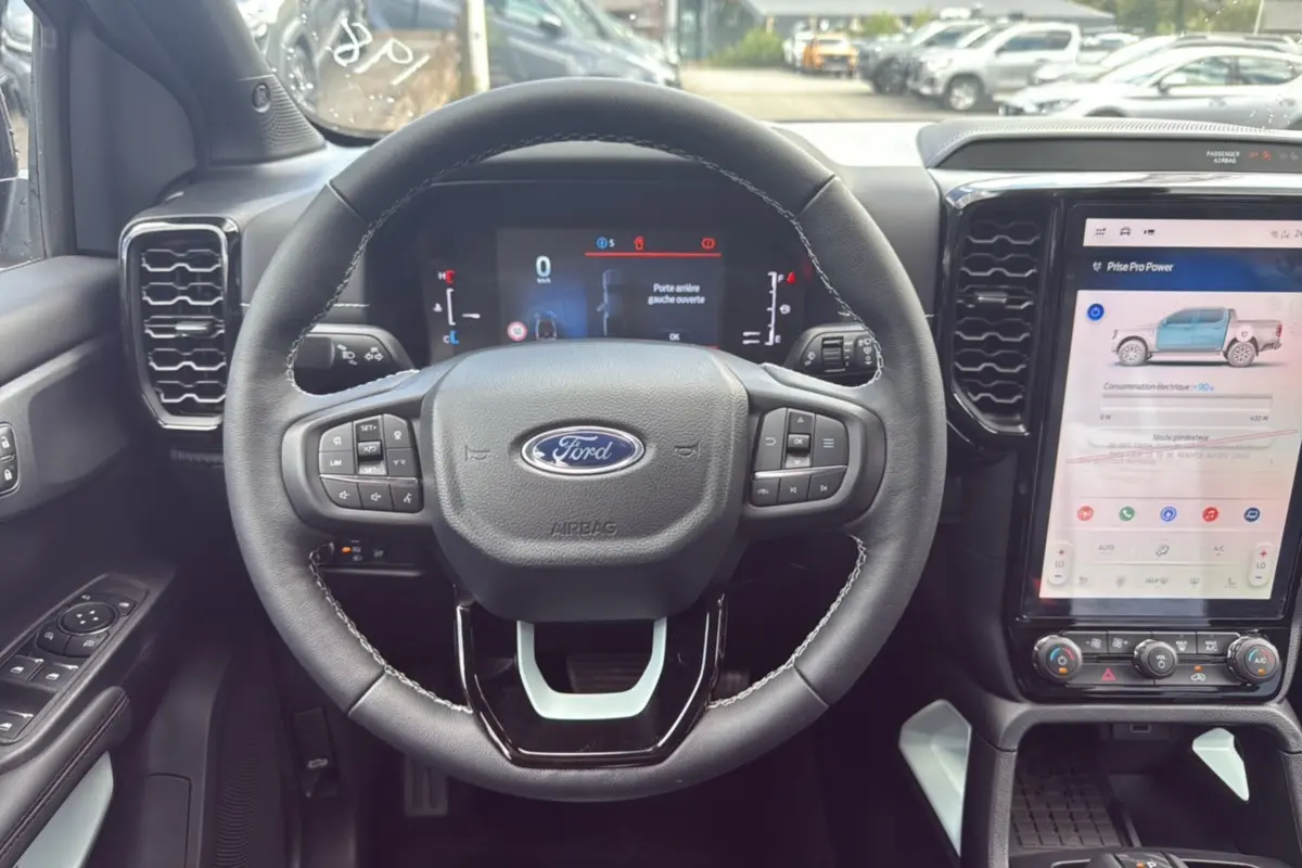 Vue intérieure centrée sur le volant cuir multifonctions d’un Ford Ranger 2.3 PHEV avec écran tactile et commandes au volant.