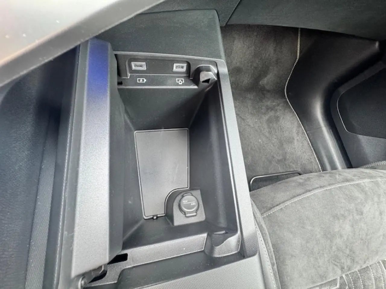 Gros plan de la console centrale noire avec prises USB et prise 12V dans le Peugeot 3008 blanc nacré 2024.