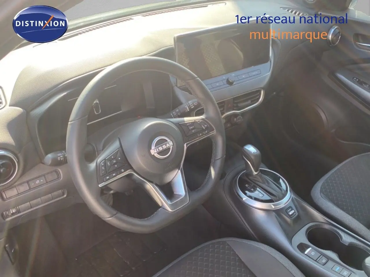 Vue intérieure centrée sur le volant Nissan et la console centrale du Juke 1.6 Full Hybrid avec sellerie noire.