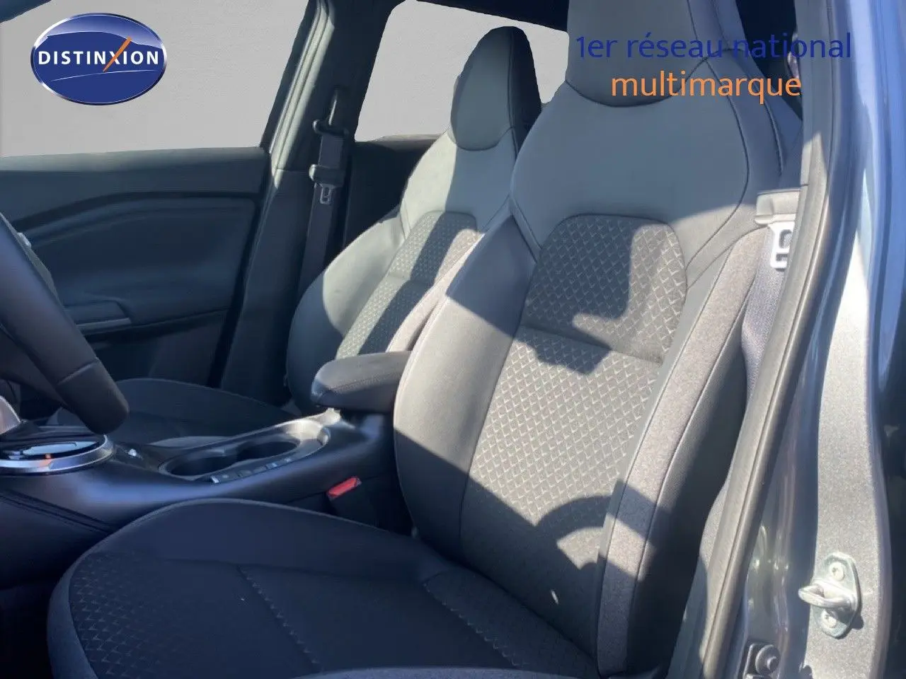 Vue intérieure côté conducteur du Nissan Juke 2025, sièges tissu noir gris avec motifs géométriques et accoudoir central.