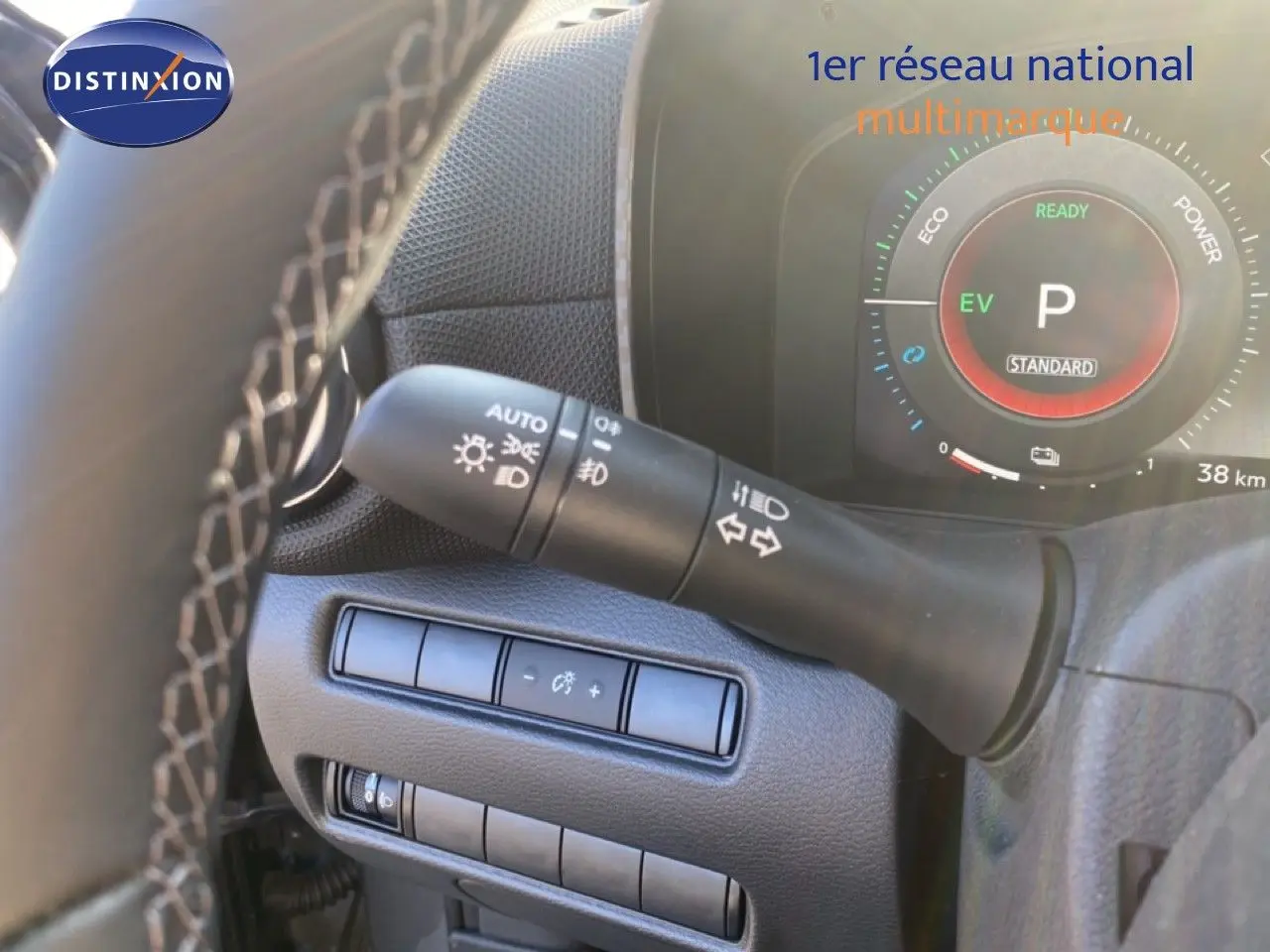 Gros plan sur le commodo d'éclairage et le tableau de bord numérique du Nissan Juke hybride, intérieur noir.
