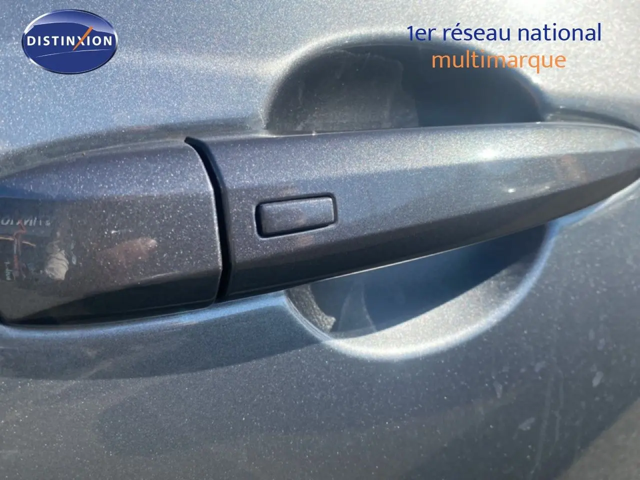 Poignée de porte avant gauche gris squale métal du Nissan Juke 2025 avec bouton de déverrouillage intégré.
