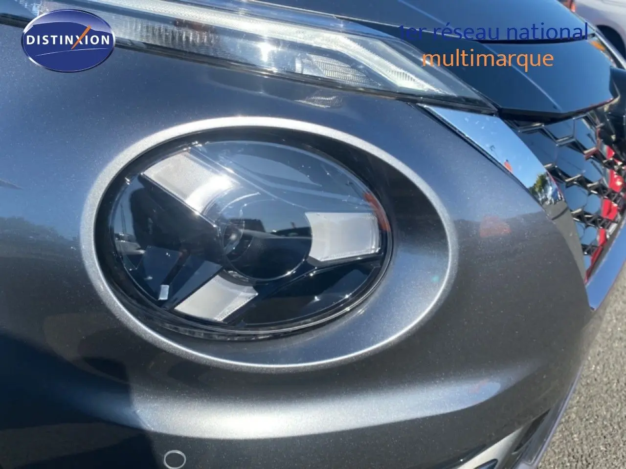 Gros plan sur le phare avant droit du Nissan Juke 2025 gris squale métal avec calandre noire brillante.