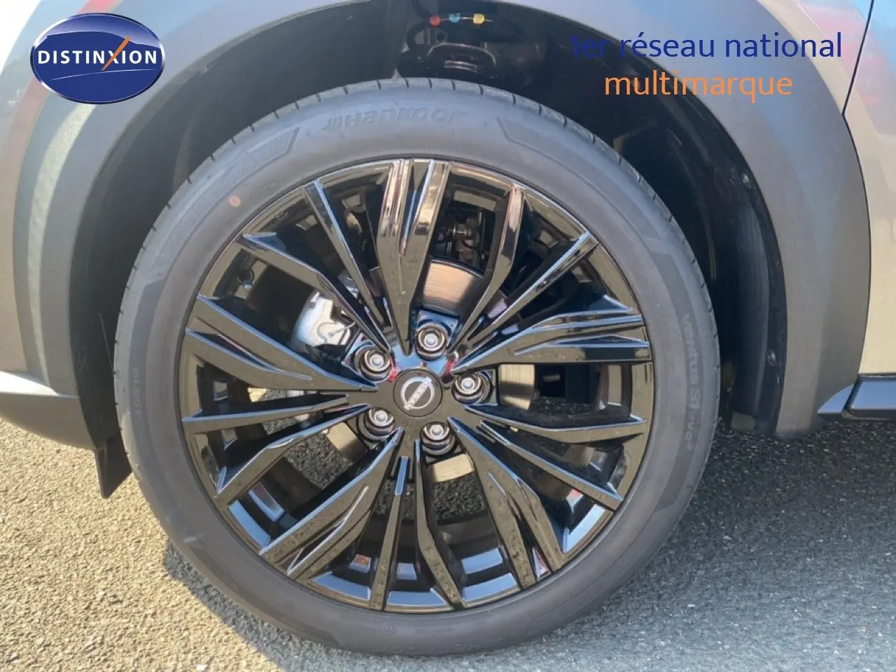 Gros plan sur la roue avant droite du Nissan Juke 2025, jante noire brillante avec carrosserie gris squale métal visible.