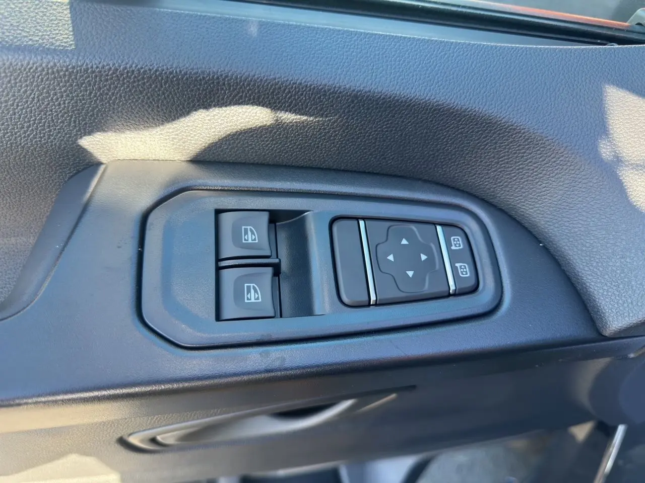 Gros plan sur les commandes électriques des vitres et rétroviseurs sur la porte intérieure côté conducteur du Renault Trafic Combi gris.