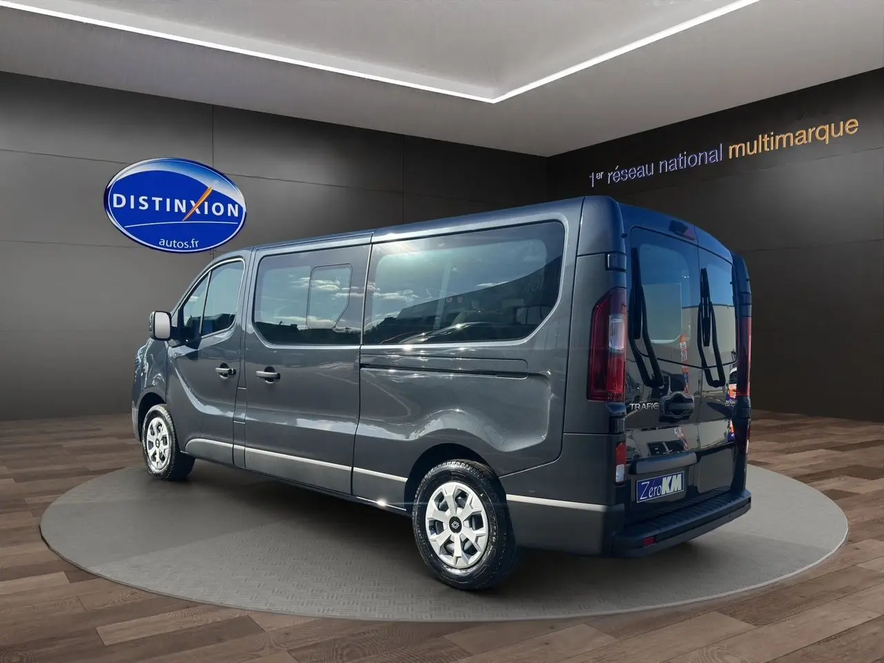 Vue 3/4 arrière droite d'un Renault Trafic Combi gris comète avec portes arrière vitrées dans un showroom.