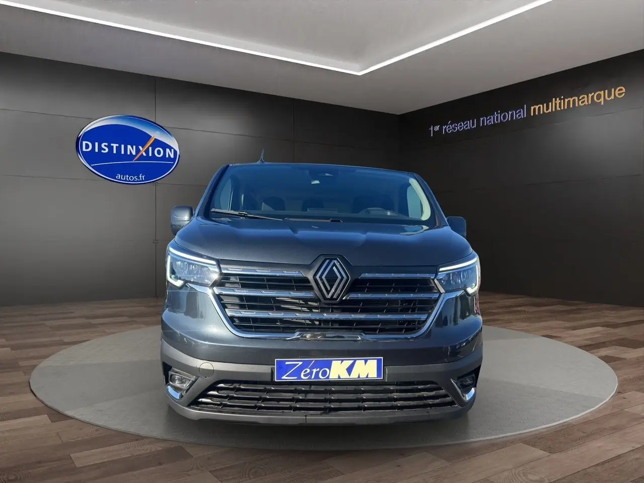 Renault Trafic Combi gris comète vu de face, avec calandre chromée et feux LED intégrés allumés.