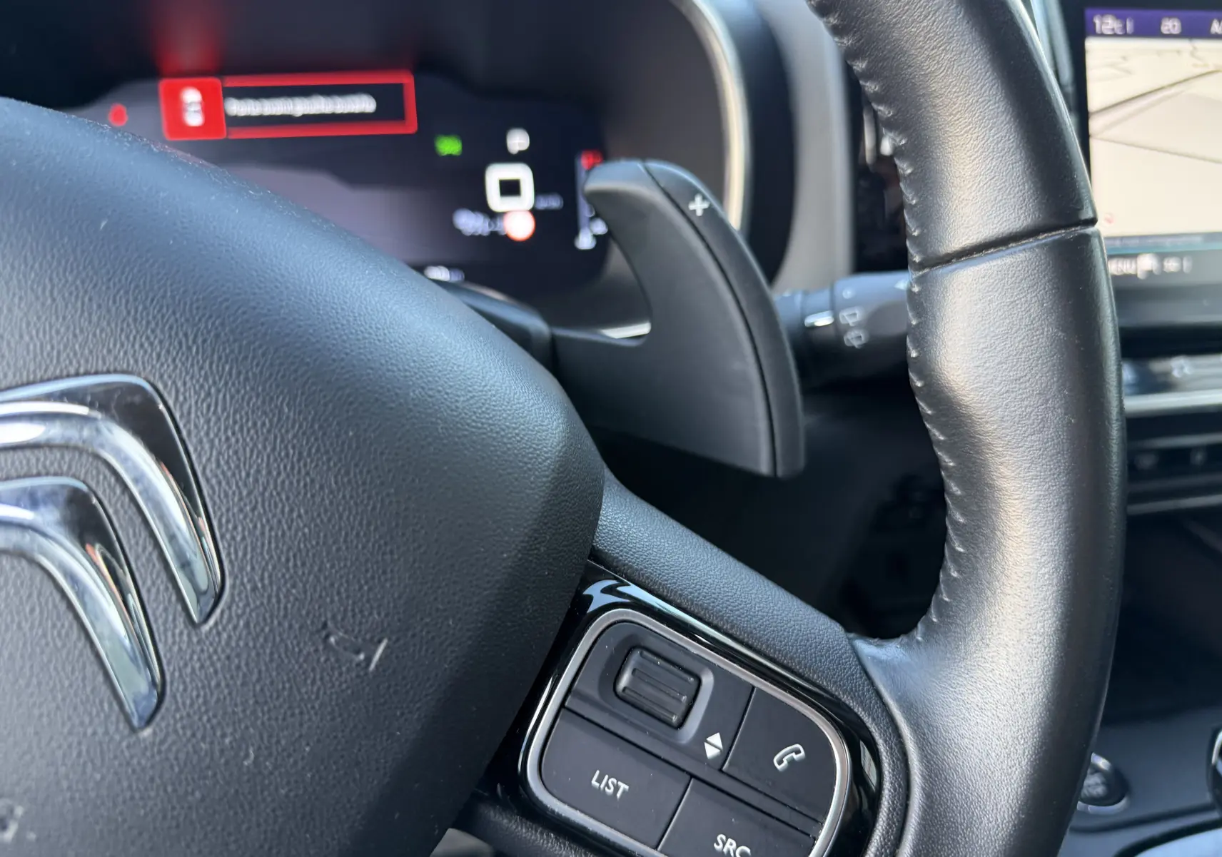 Gros plan sur le volant en cuir noir du Citroën C5 Aircross 2021, avec commandes intégrées et tableau de bord numérique flou.