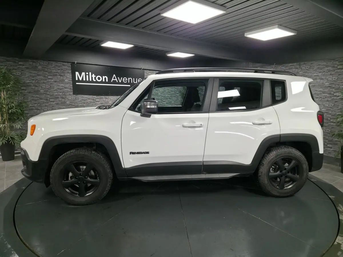 Profil côté gauche d'un Jeep Renegade blanc 2018 avec jantes noires 5 branches et barres de toit gris clair.