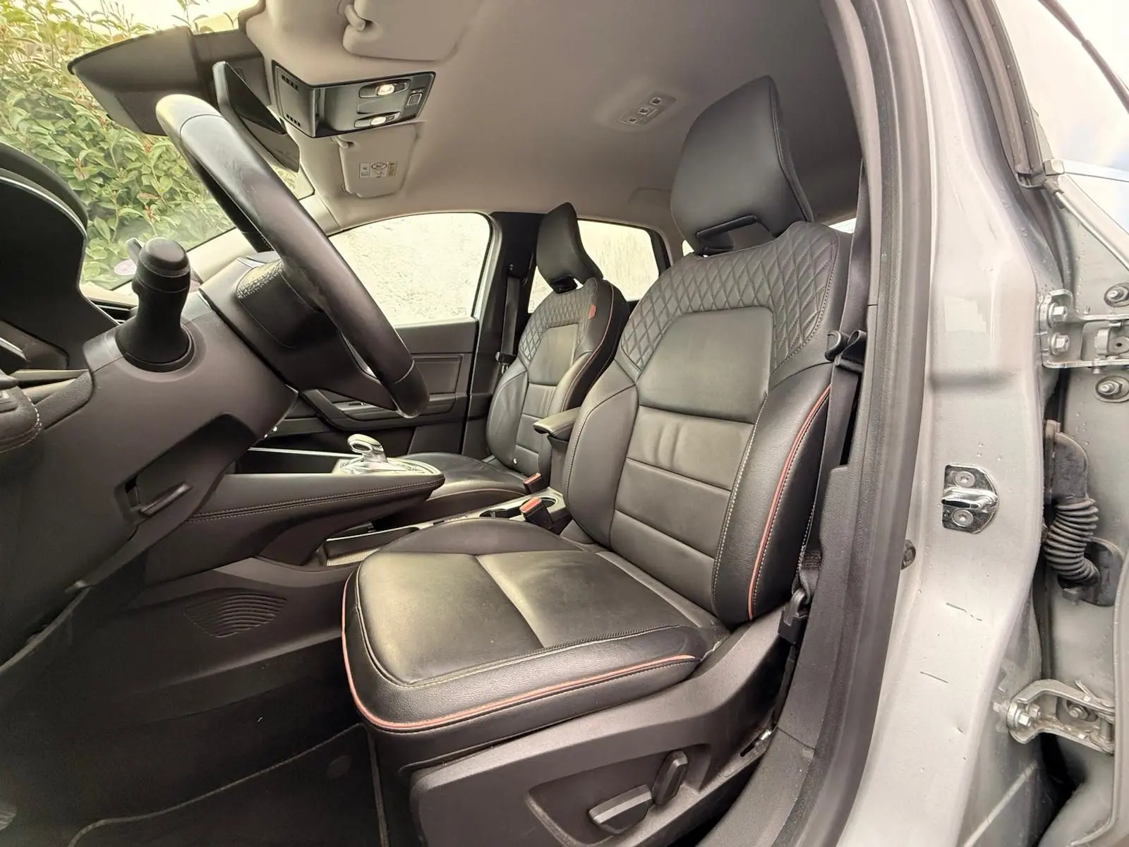 Intérieur de la Renault Captur gris Highland, vue côté conducteur sur les sièges en cuir noir avec surpiqûres rouges.