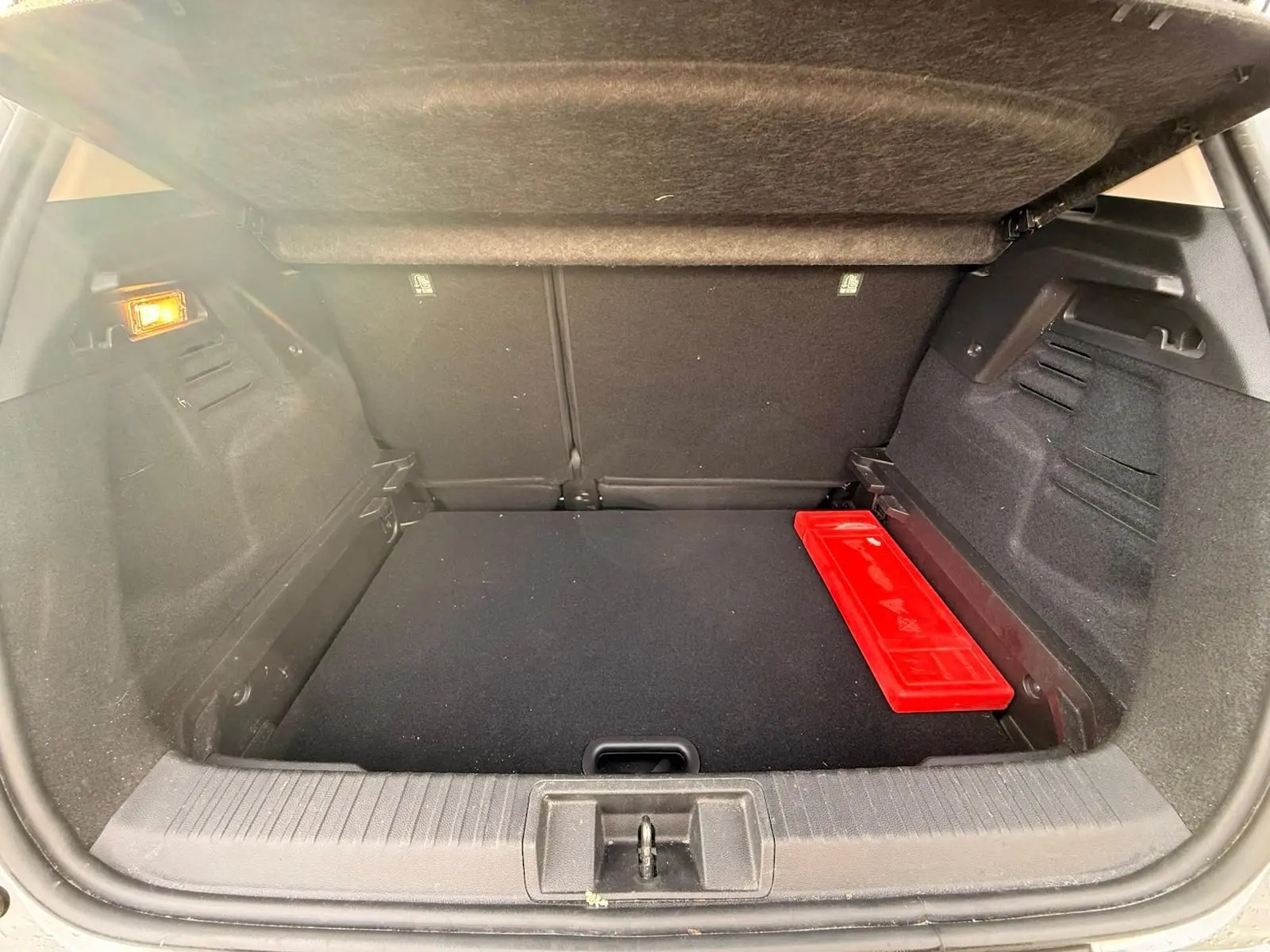 Coffre ouvert du Renault Captur gris Highland, vue intérieure arrière avec un triangle de signalisation rouge posé à droite.