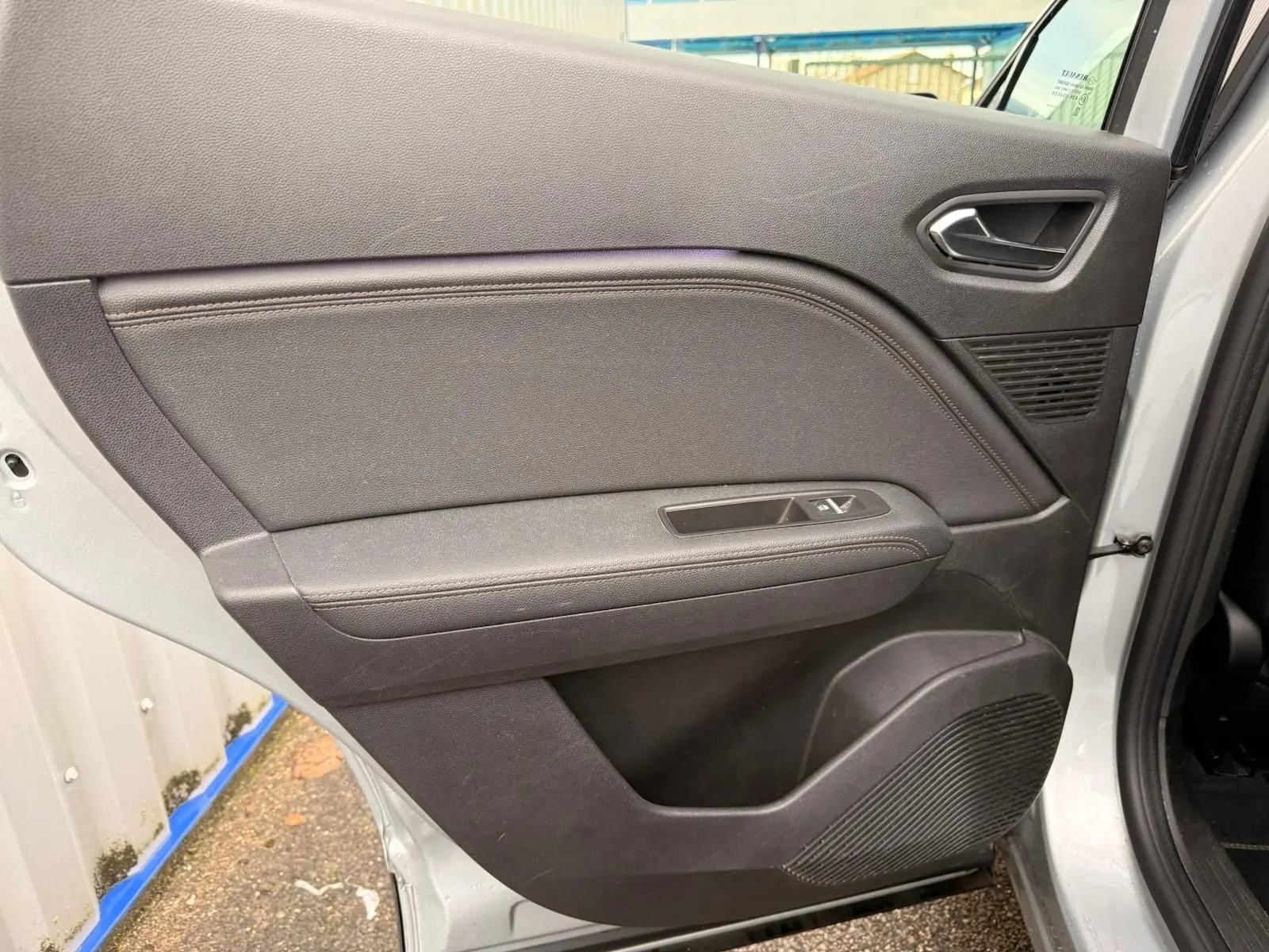 Vue intérieure de la porte arrière droite du Renault Captur gris Highland, avec commandes de fenêtre et haut-parleur intégré.
