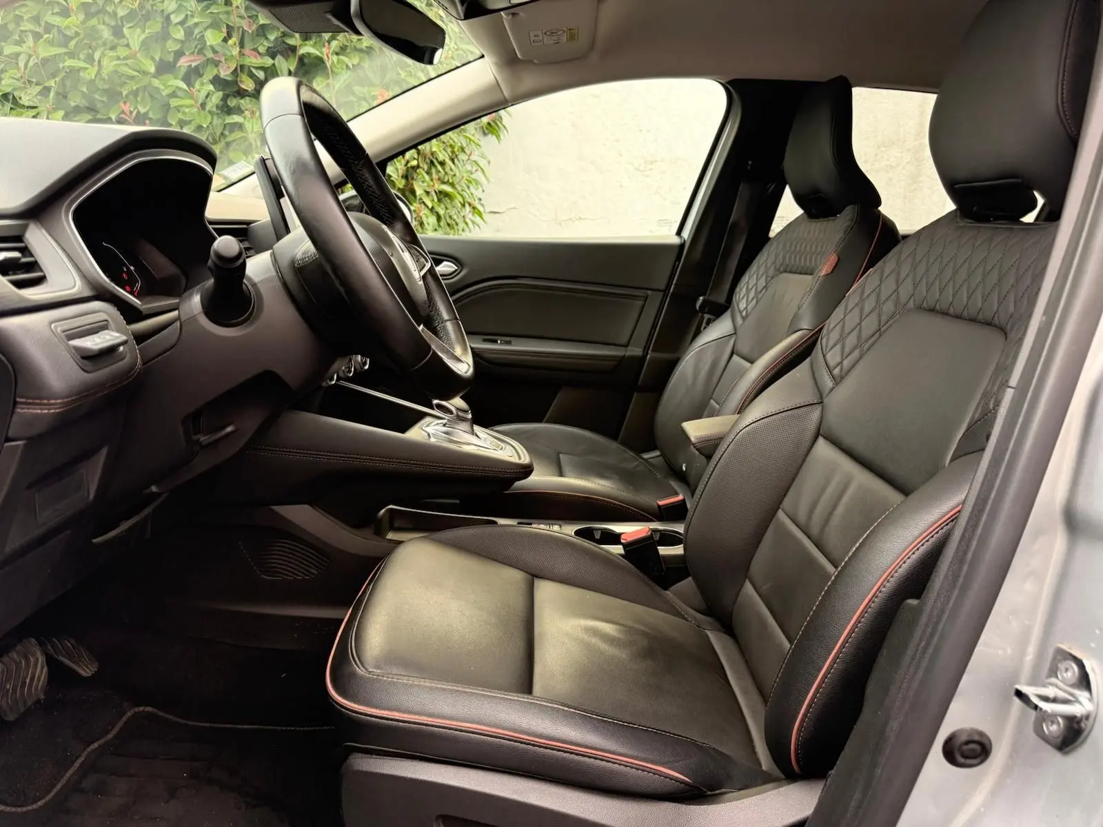Intérieur du Renault Captur 1.6 E-TECH hybride 2021, vue côté gauche sur sièges cuir noirs avec surpiqûres rouges.