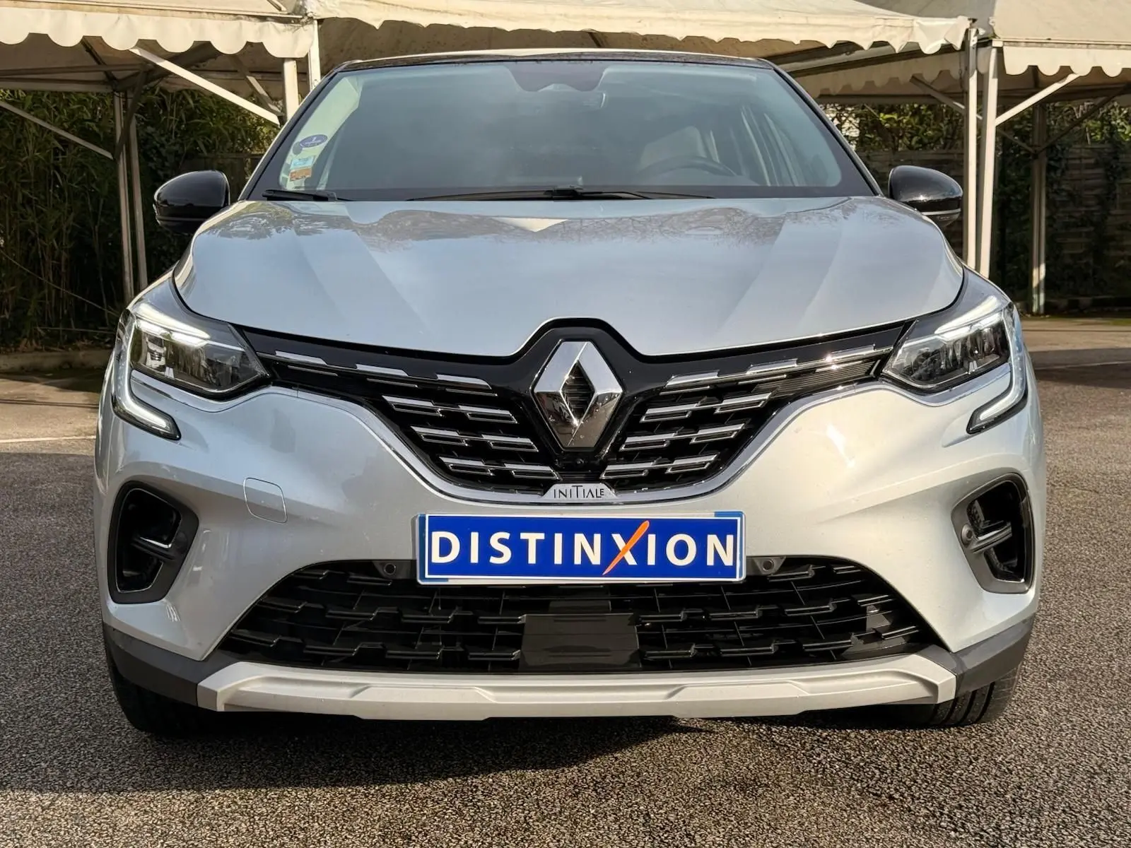 Vue frontale d'un Renault Captur gris Highland avec calandre noire et logo chromé sous un auvent.