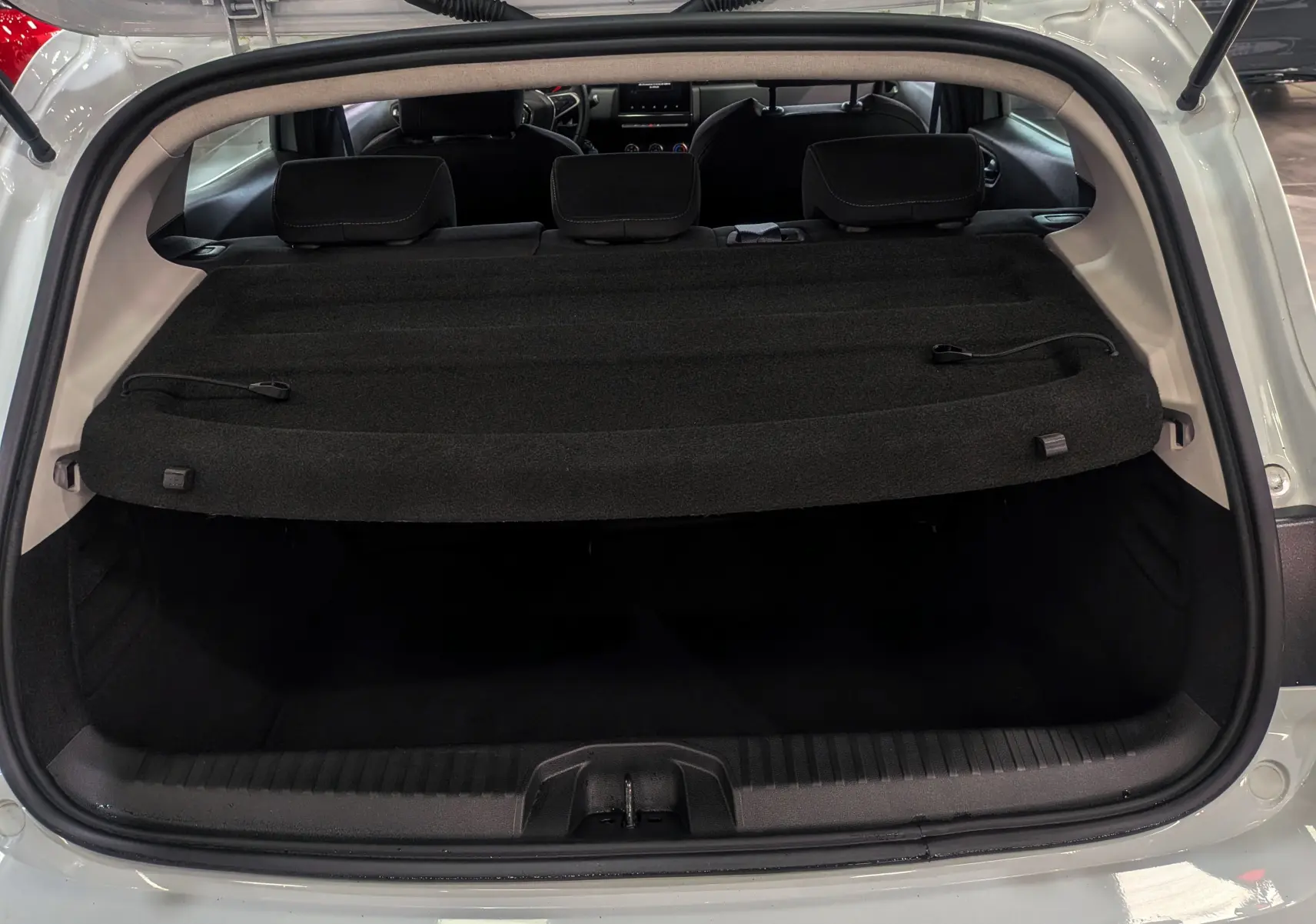 Coffre ouvert vu de l'arrière d'une Renault Clio V Blanc Glacier, avec cache-bagages et sièges arrière visibles.