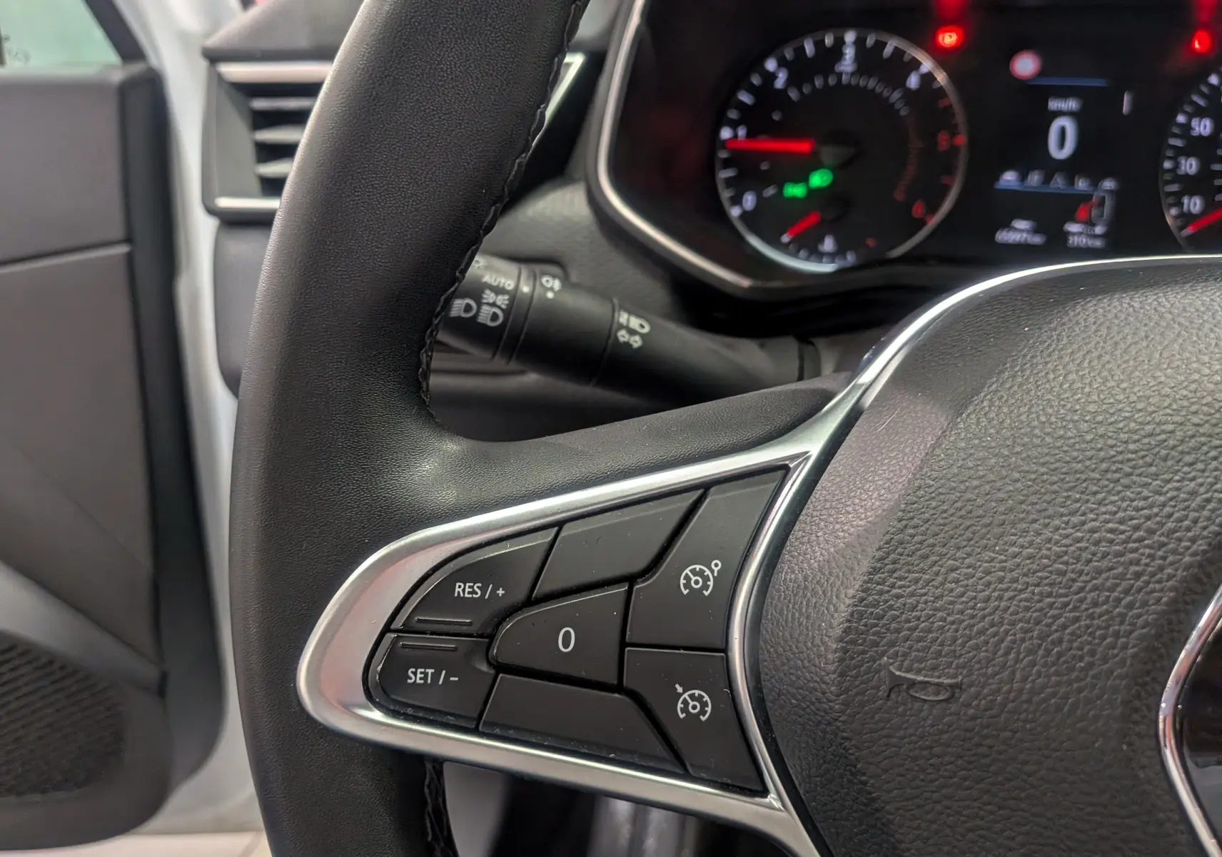 Gros plan sur le volant noir de la Renault Clio V, montrant les commandes de régulateur de vitesse et le tableau de bord en arrière-plan.