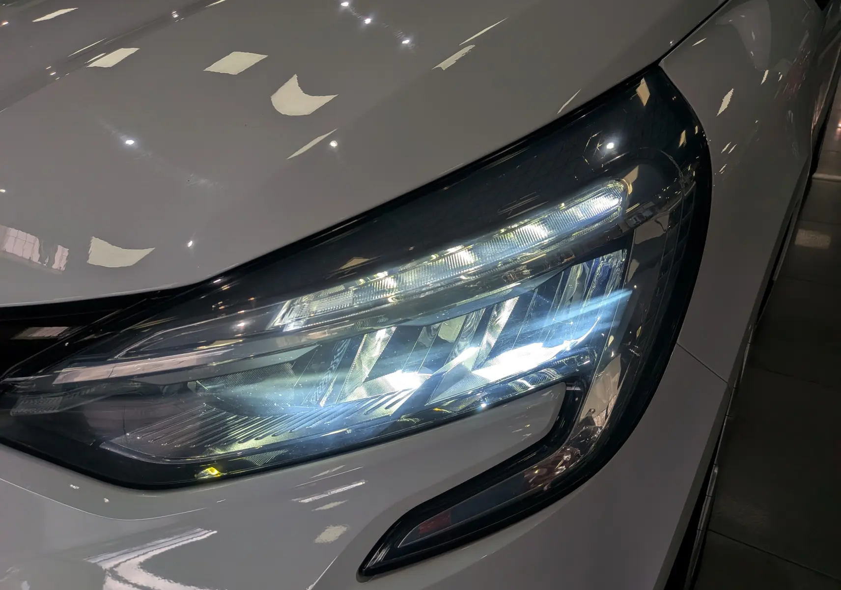 Gros plan sur le phare avant droit allumé d'une Renault Clio V Blanc Glacier, soulignant son design moderne et lumineux.