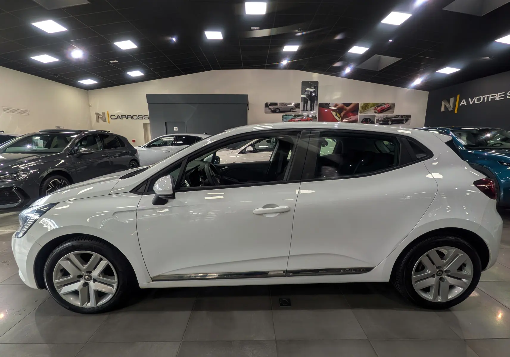 Profil côté gauche d'une Renault Clio V Blanc Glacier 2020 en intérieur, soulignant ses jantes et lignes épurées.