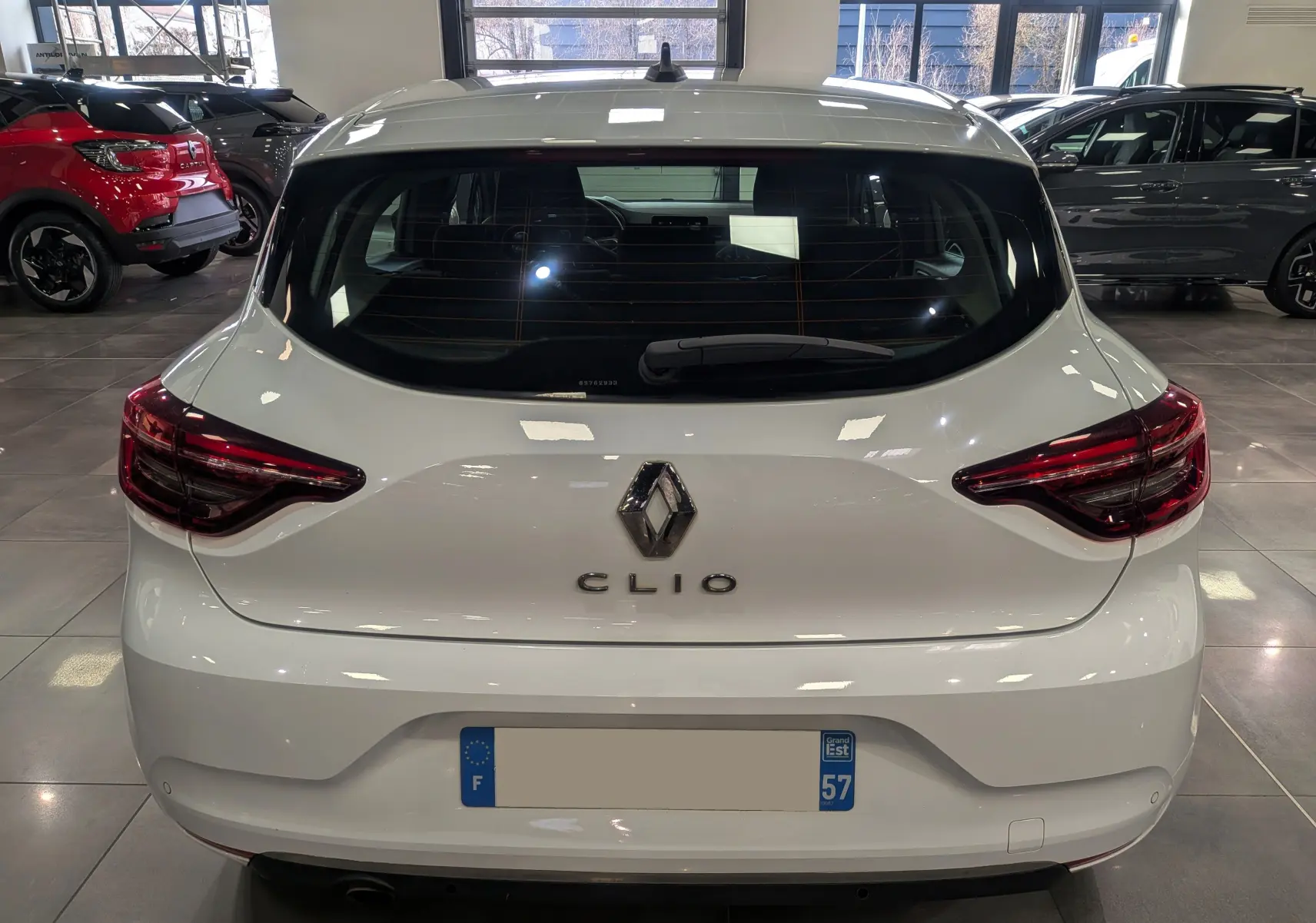 Vue arrière d'une Renault Clio V Blanc Glacier 2020 dans un showroom, avec feux arrière LED et logo central visible.
