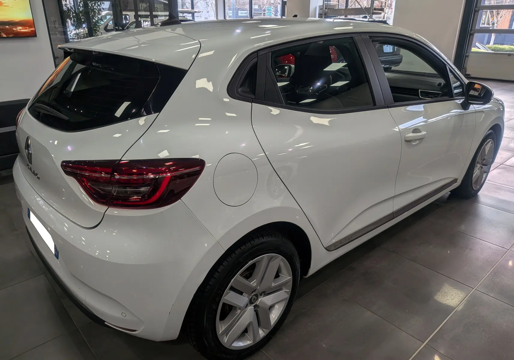 Vue 3/4 arrière droite d'une Renault Clio V Business Blanc Glacier, avec feux arrière LED et jantes alliage visibles.