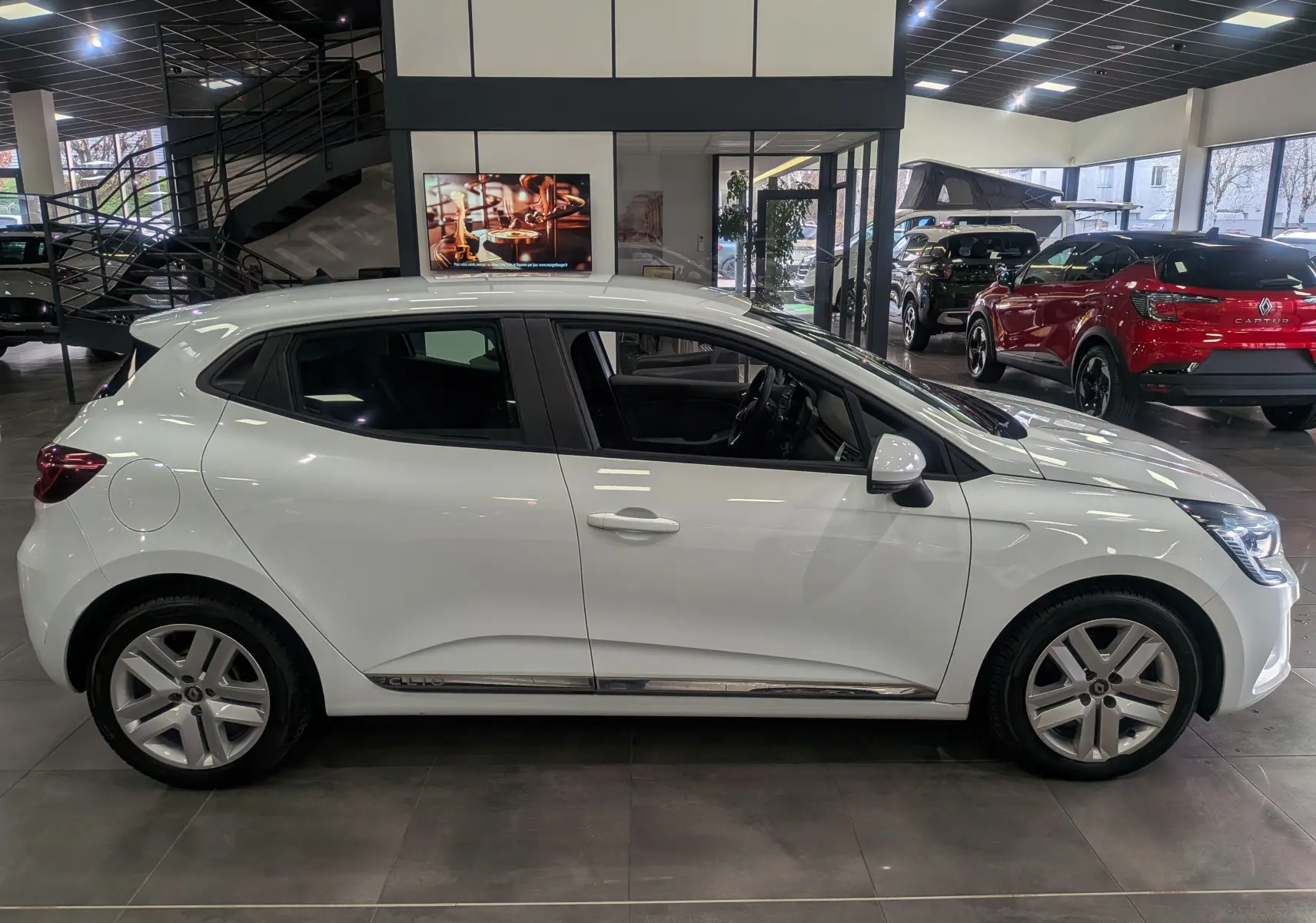 Renault Clio V Blue dCi 85 CH BUSINESS blanc glacier vue de profil côté gauche en intérieur de showroom.